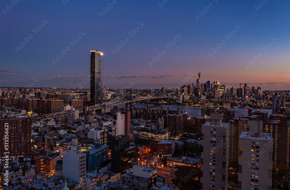 Aerial view of Manhattan Bridge and surrounding buildings in urban neighbourhoods on both riverbanks after sunset. Evening city scene. Manhattan, New York City, USA