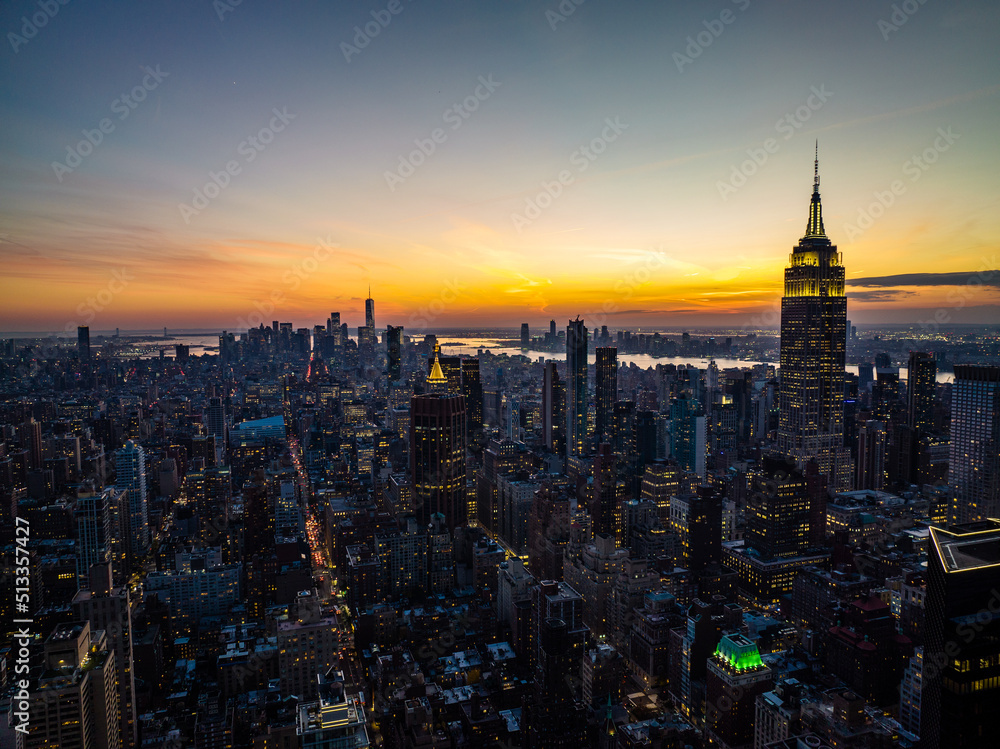 Naklejka premium High rise buildings in arranged in blocks surrounded with streets. Cityscape against colourful sunset sky. Manhattan, New York City, USA