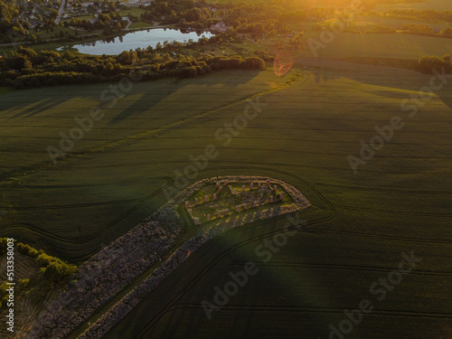 Aerial view with beautiful cereal field at sunset with a huge stone house in the middle of the field. The building resembles stonehenge. Smiltene stonehenge, Latvia