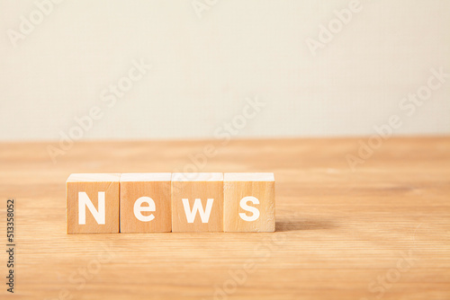 Newsの文字。ニュース。新着情報。木製のテーブルの上に置かれた4つの木製ブロックに書かれている。白い文字。