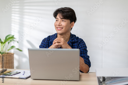 Entrepreneur handsome business asian man wear blue shirt working online on desk table smile and happiness with laptop at home.Attractive Freelance man working online sale marketing at home office