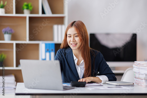 Asian Business woman using calculator and laptop for doing math finance on an office desk, tax, report, accounting, statistics, and analytical research concept