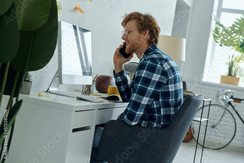 Confident young man talking on mobile phone while sitting at his working place at home