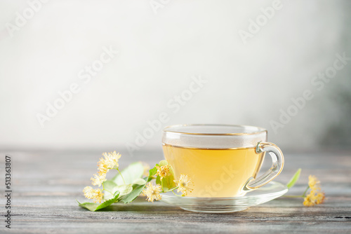 Glass teacup of green tea and linden flowers on wooden background. Herbal hot drink