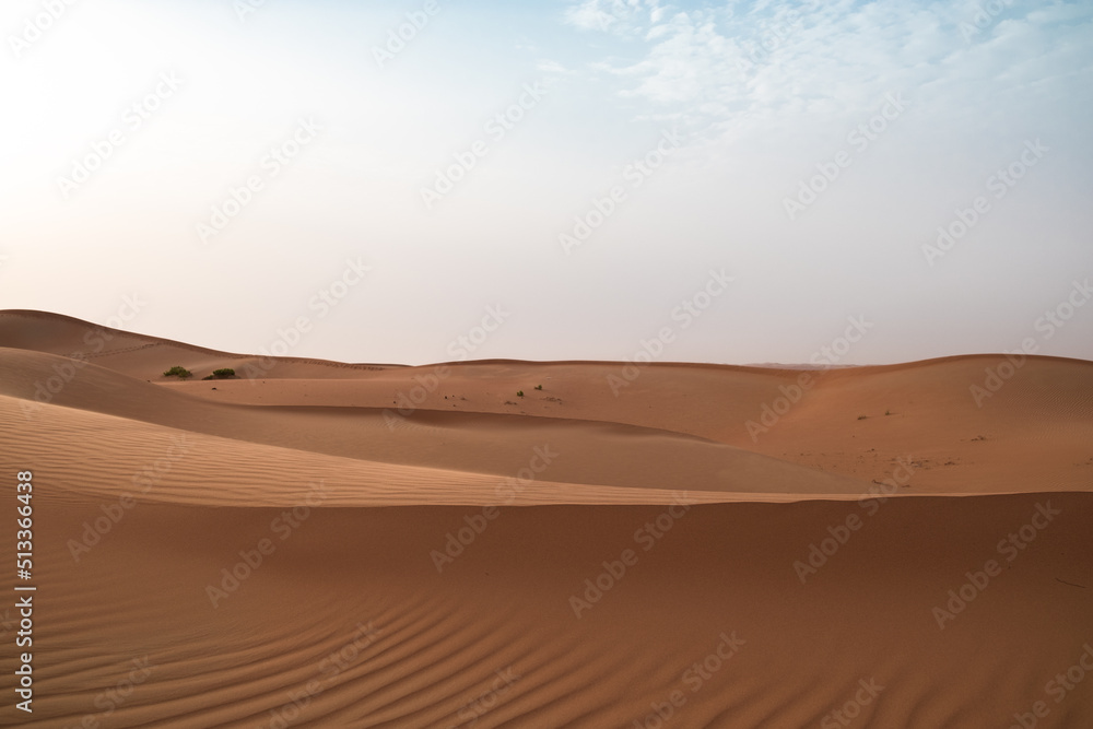 Landscape of sand dunes against a bright blue sky in Al Wathbah Desert in Abu Dhabi, United Arab Emirates.