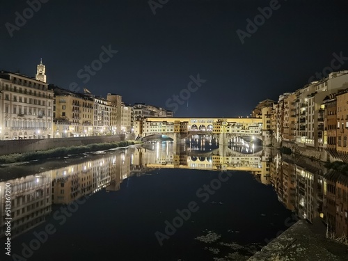 Night photo of the Arno river, in the stretch crossed by the Ponte Vecchio which is reflected in the calm water.