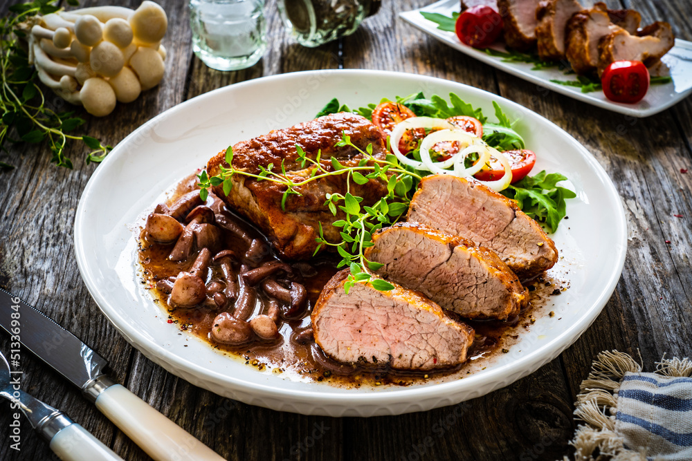 Roasted pork loin with shimeji mushrooms in sauce, fresh thyme, greens and cherry tomatoes on wooden table
Roasted pork loin with shimeji mushrooms in sauce, fresh thyme, greens and cherry tomatoes on wooden table