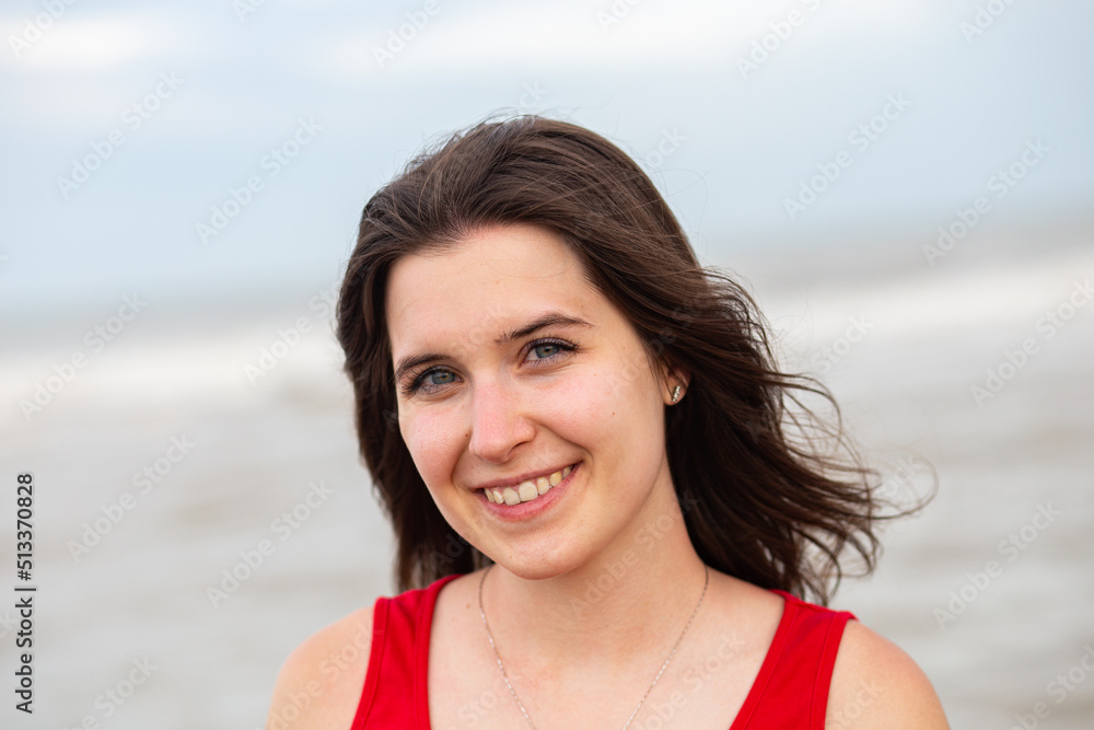 Portrait, close-up of a young smiling brunette girl in a bright red t-shirt on the beach Portrait, close-up of a young smiling brunette girl in a bright red t-shirt on the beach