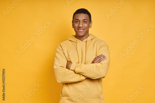 Handsome African man keeping arms crossed while standing against yellow background