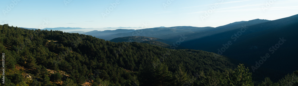 Panorama of a valley  covered by forest with sunbeams coming through the mountains