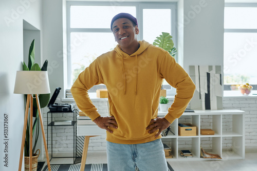 Confident African man holding hand on hip and smiling while standing at home office © gstockstudio