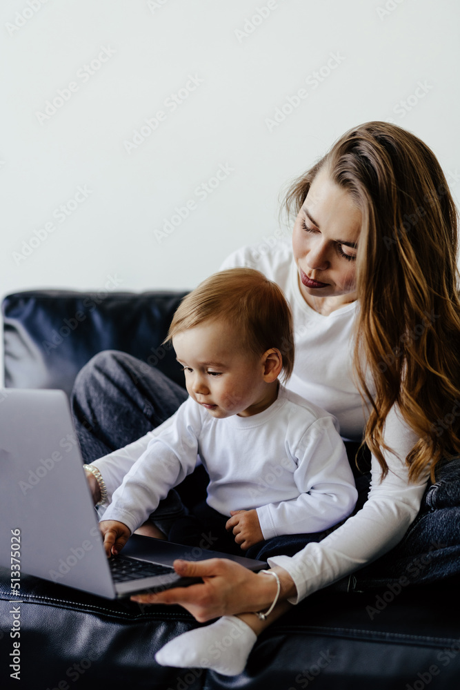 Young smiling freelancer mother pointing at laptop while holding little son Young smiling freelancer mother pointing at laptop while holding little son