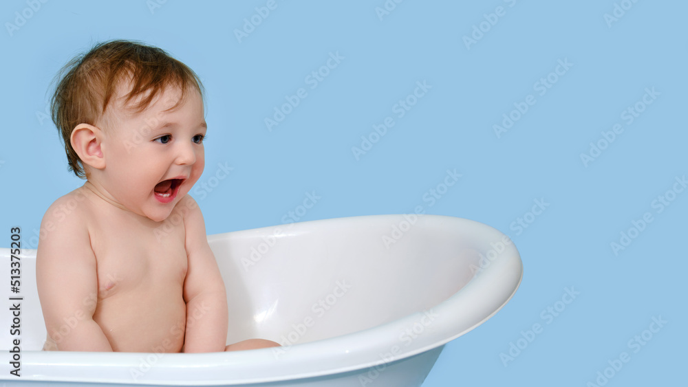 Screaming baby toddler boy is sitting in a white tub on a studio blue background. Shouting child at the age of one year, copy space Screaming baby toddler boy is sitting in a white tub on a studio blue background. Shouting child at the age of one year, copy space