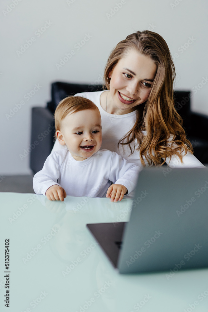 Young beautiful woman multitasking, working from home teaching two year old son to draw. Woman spending quality time with her toddler child. Homeschooling concept. Young beautiful woman multitasking, working from home teaching two year old son to draw. Woman spending quality time with her toddler child. Homeschooling concept.