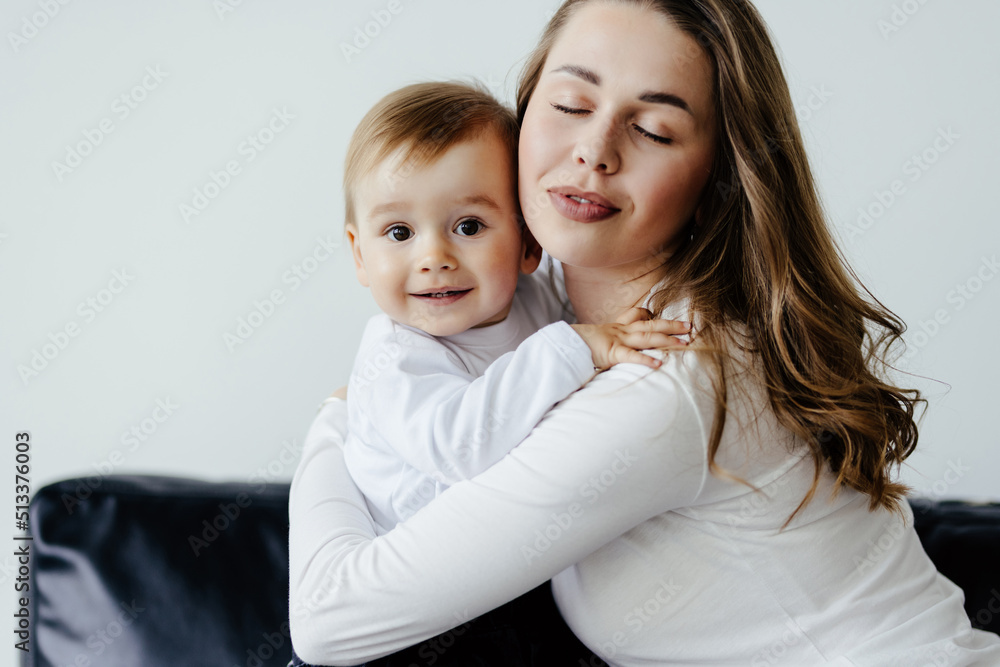 Young woman cuddling talking to small kid son, having fun together on couch in studio living room. Smiling child boy communicating with elder sister nanny babysitter, laughing at home. Young woman cuddling talking to small kid son, having fun together on couch in studio living room. Smiling child boy communicating with elder sister nanny babysitter, laughing at home.
