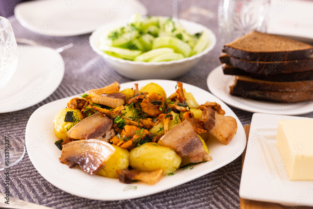 baked potatoes with chanterelles and bacon served with herbs and lightly salted cucumbers on table baked potatoes with chanterelles and bacon served with herbs and lightly salted cucumbers on table