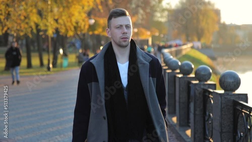 Stylish, handsome young Caucasian man walks along the embankment after work. A confident and successful guy walks by the river. Slow motion. High quality FullHD footage