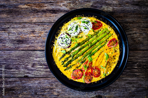 Tasty breakfast. Omelette  with green asparagus, goat cheese, pepper and cherry tomatoes served on black plate on wooden table
