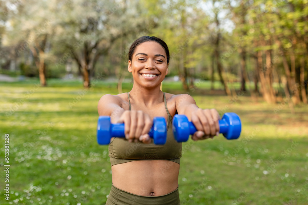 Smiling young black woman doing outdoor strength training, exercising with dumbbells at park, copy space Smiling young black woman doing outdoor strength training, exercising with dumbbells at park, copy space