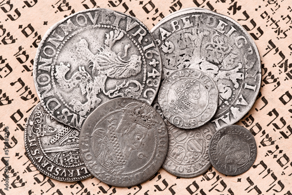 Heap of old silver coins on open Siddur page. Selective focus. Closeup.