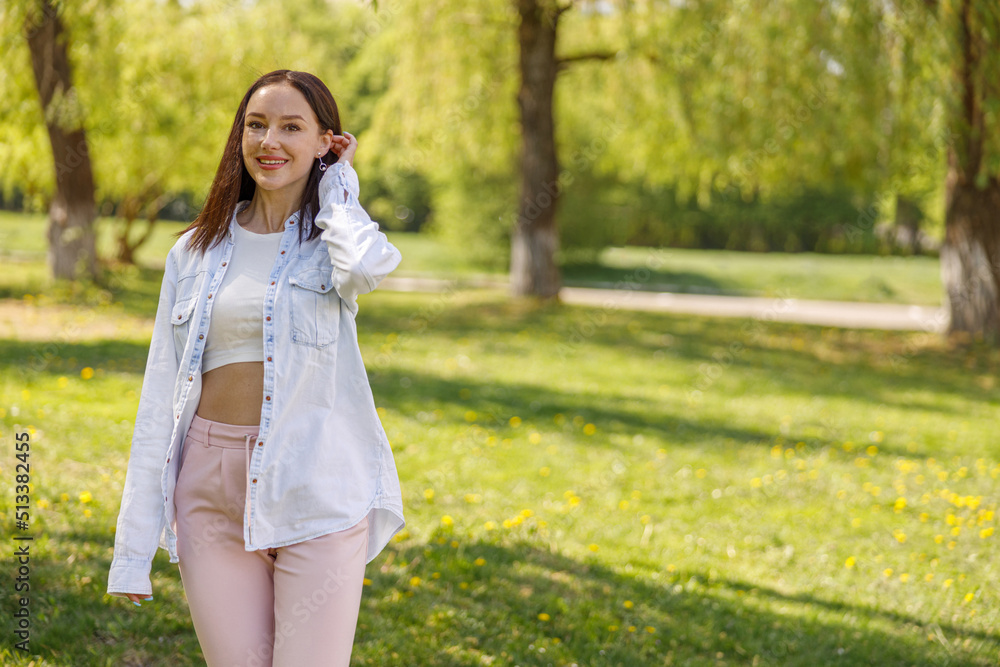 Beautiful cheerful young brunette woman standing in green park and smiling to camera. Beautiful cheerful young brunette woman standing in green park and smiling to camera.