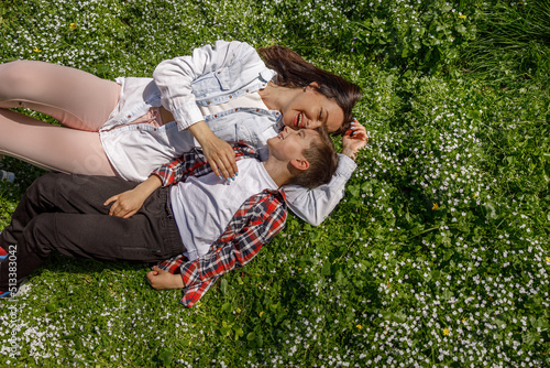 View from above on happy cheerful mother and son lying on green grass, hugging nose to nose.