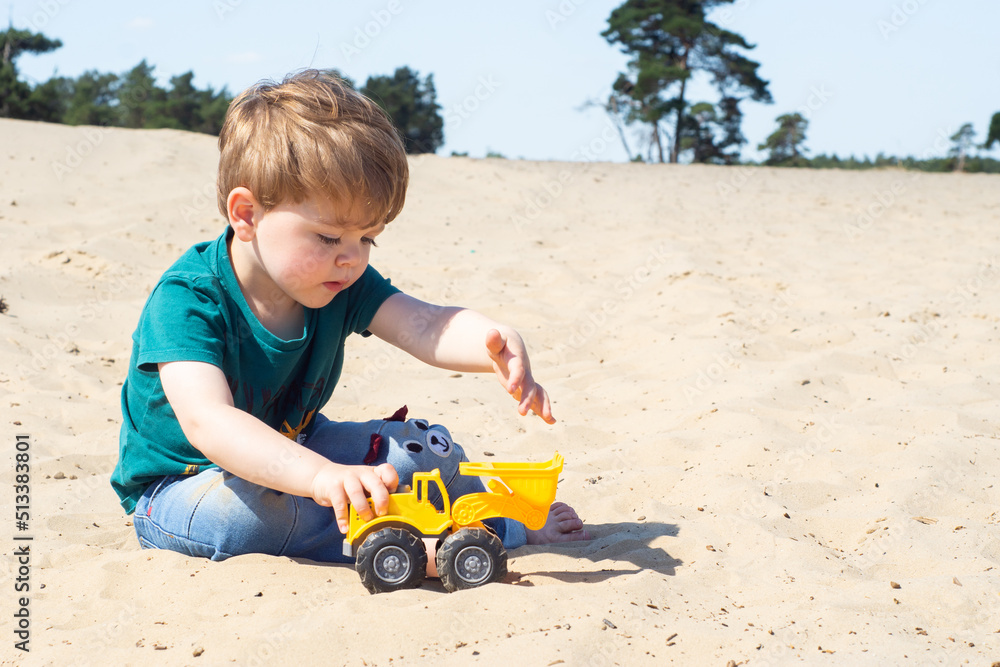 Little caucasian toddler boy playing a yellow toy excavator on a sandy beach. A cute child enjoying building from sand. Little caucasian toddler boy playing a yellow toy excavator on a sandy beach. A cute child enjoying building from sand.
