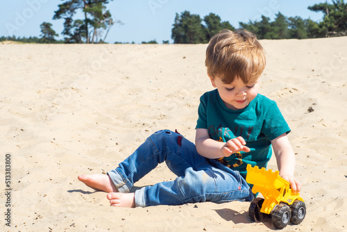 Obraz na płótnie Little caucasian toddler boy playing a yellow toy excavator on a sandy beach. A cute child enjoying building from sand. w salonie
