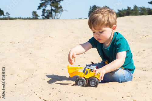 Obraz na płótnie Little caucasian toddler boy playing a yellow toy excavator on a sandy beach. A cute child enjoying building from sand. w salonie