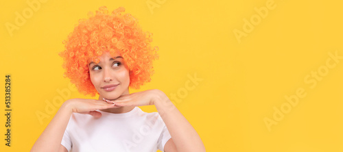 cute funny girl with fancy look wearing orange hair wig on yellow background, party. Woman isolated face portrait, banner with copy space.