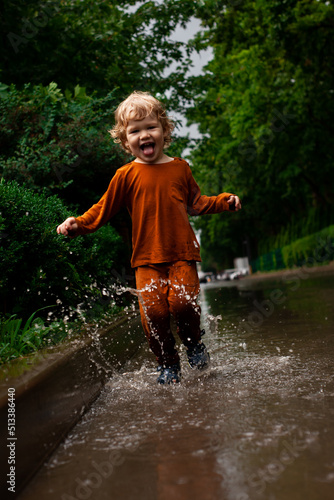 Fototapeta Naklejka Na Ścianę i Meble -  a little boy runs and jumps in the puddles during the summer rain.Childhood.