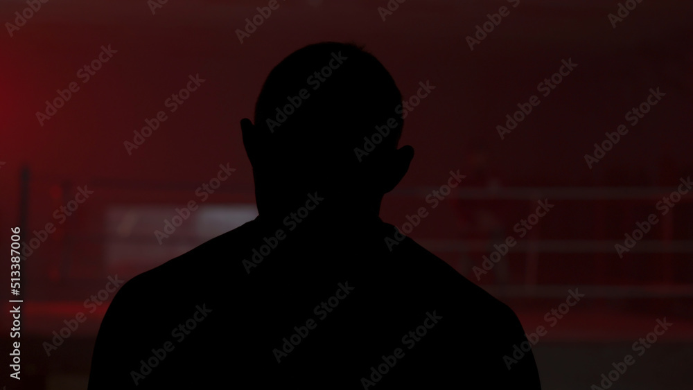 Silhouette of a man who comes into the room with a red light, back view. Shadow of man in the red room. Silhouette of a man in the light