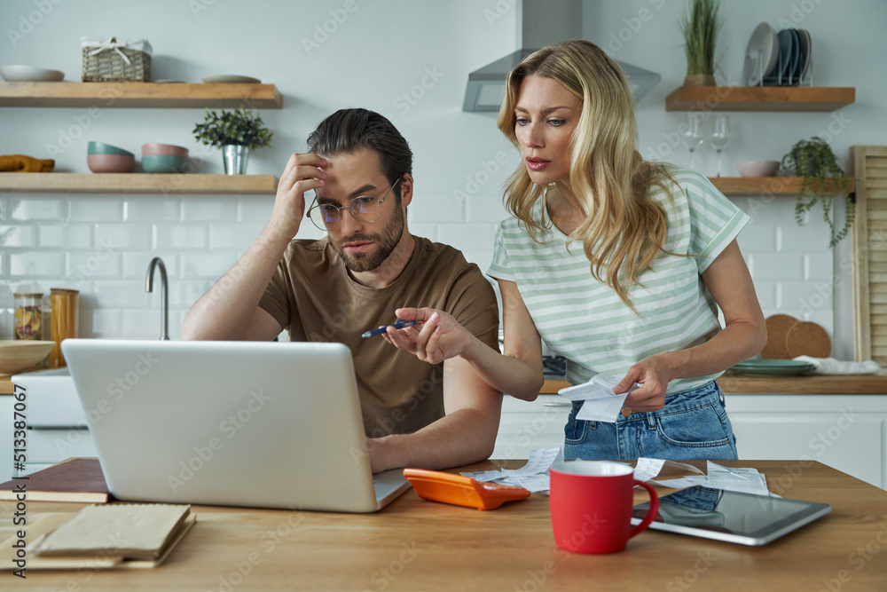 Young couple calculating finances while sitting at the domestic kitchen Young couple calculating finances while sitting at the domestic kitchen