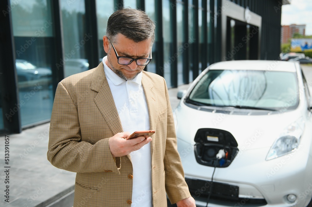 Handsome man using phone while car being charged Handsome man using phone while car being charged
