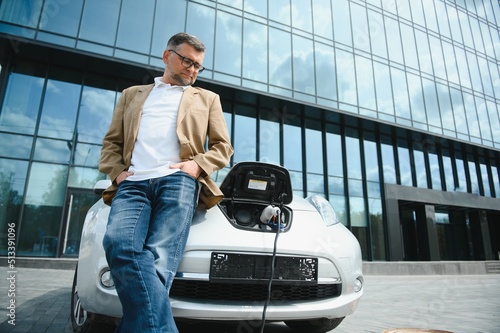 Handsome man while charging electric car. © Serhii