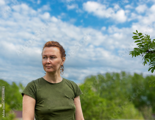 a woman in the countryside without makeup with a serious face. background blue sky and green trees