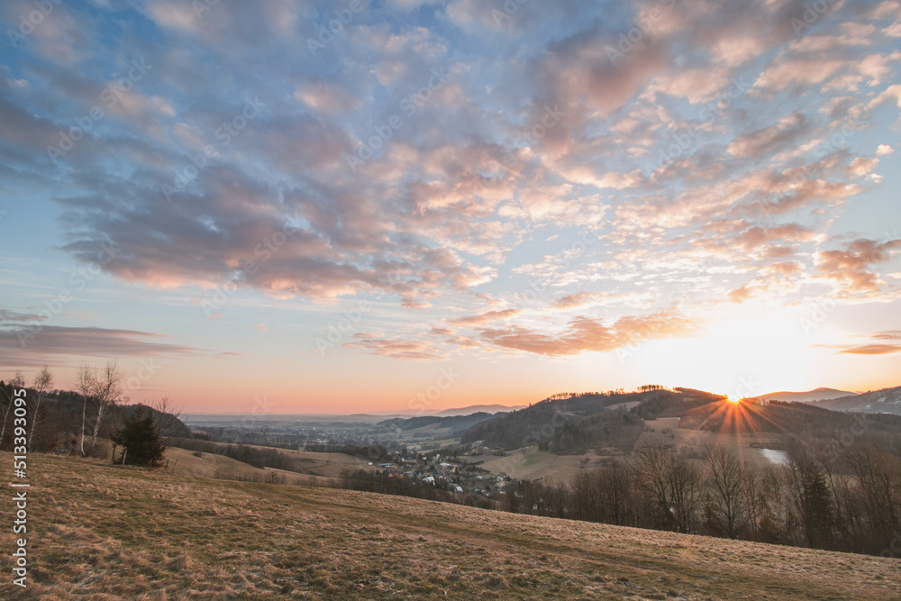 Sunrise at the hills of the mountains and the village of Kozlovice in the foothills of the Beskydy Mountains in the Moravian-Silesian region of the Czech Republic. Colorful clouds with orange ball