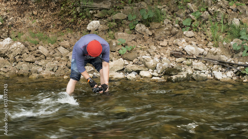 Man with a camera standing in a rocky river and taking pictures of the water surface. Stock footage. Male hiker with a camera shooting videos of the forest stream.