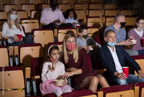 parents and children in masks sitting at movie in cinema