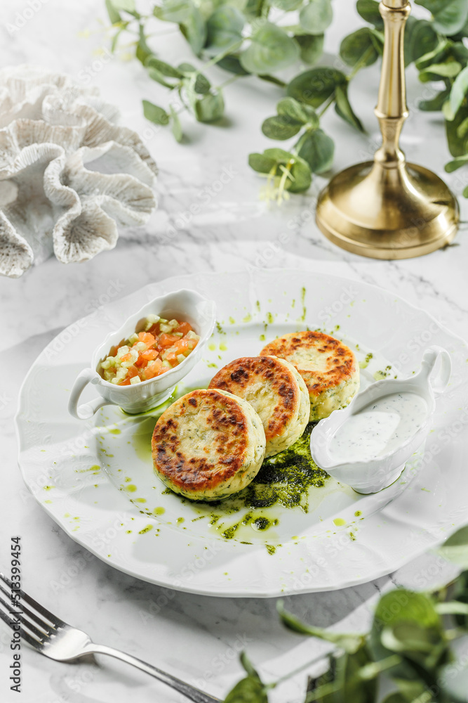 Breakfast delicious concept - cheese Pancakes with green sauce, cream sauce and fresh sliced vegetables in the white plate on light marble background. Healthy sea food, hard light, restaurant decor