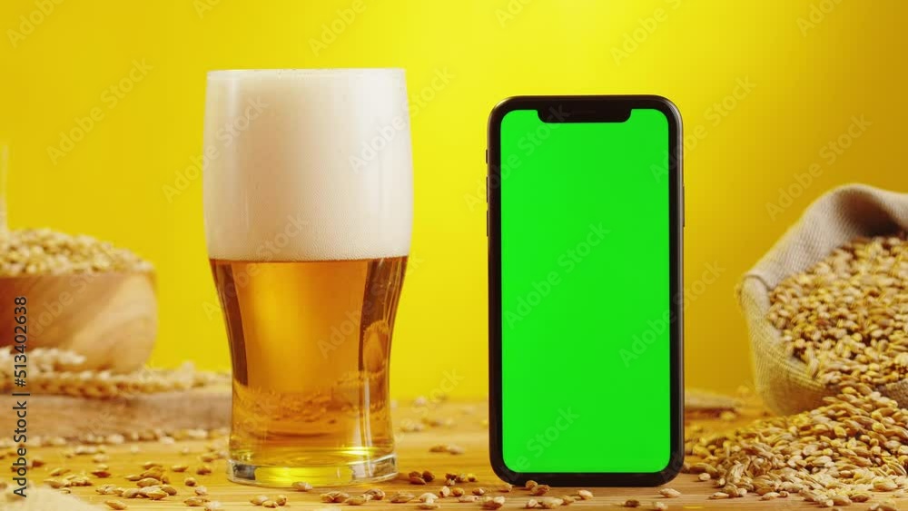 Foamy beer in glass and phone with green chroma key screen. Alcohol ...