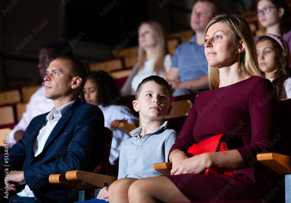 mother, father and their children sitting at perfomance in theatrical auditorium - obrazy, fototapety, plakaty 