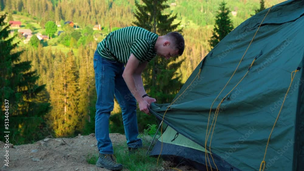Young male hiker puts a tent in the mountains. The tourist sets up a camp on a hike. Camping man outdoor lifestyle man putting up a tent in nature in forest. Young male hiker puts a tent in the mountains. The tourist sets up a camp on a hike. Camping man outdoor lifestyle man putting up a tent in nature in forest.