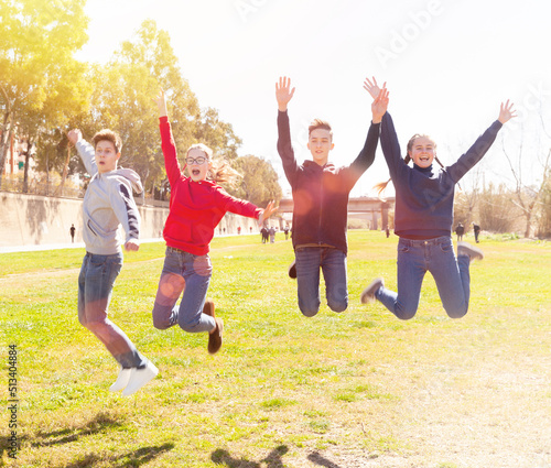 Friendly teenagers jumping together in park on spring