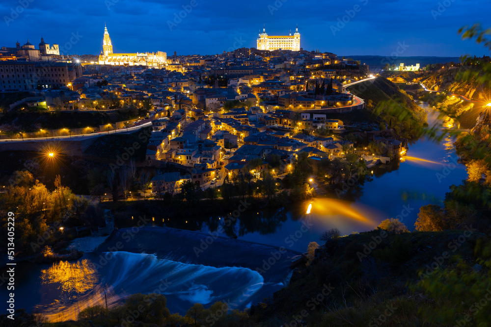 Cityscape of illuminated Toledo in evening with view of Alcazar and Tagus River. Castilla-La Mancha, Spain.