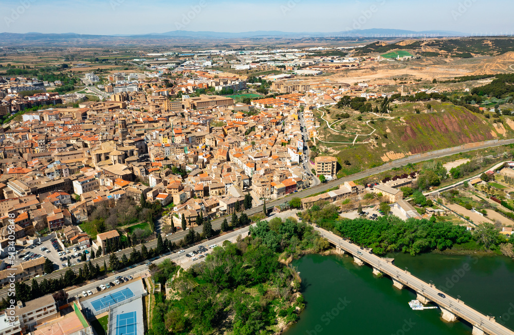 Picturesque aerial view of historic center of Tudela with brownish tiled roofs of residential buildings, medieval Cathedral of Saint Mary and ancient arched bridge over Ebro river on spring day, Spain