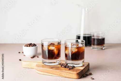 Wooden board with cold brew and coffee beans on color table against light background