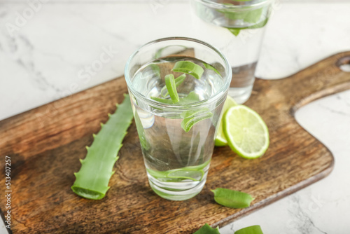 Board with glasses of aloe juice and leaves on white background