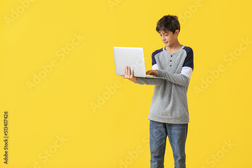 Teenage boy using laptop on yellow background