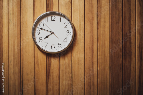 A silver clock hung on a brown wooden wall at 7 o'clock 48 minutes.